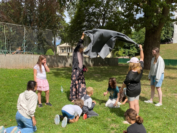 Boizenburg - draußen Eine Gruppe Kinder spielt auf einer Sommerwiese, zwei Erwachsene stehen und ziehen gerade eine Decke nach oben