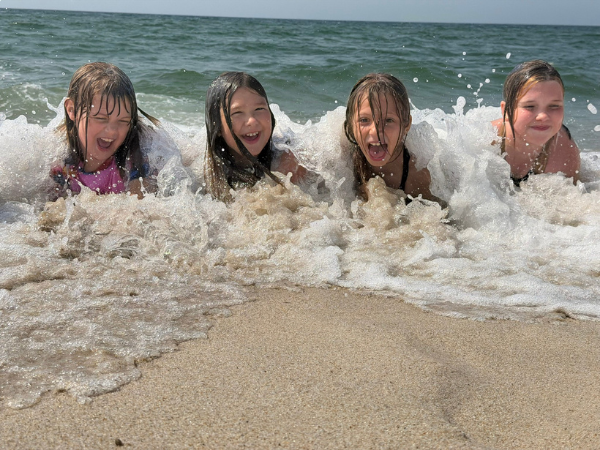 Puan 2 - Badespass Vier Mädchen liegen auf dem Bauch im Meer und lassen sich von den Wellen abkühlen, alle lachen in die Kamera
