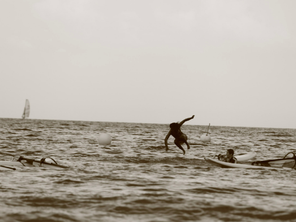 Surf-Camp - im Wasser Ein Jugendlicher springt von einem Surfbrett ins Wasser, ein anderer liegt auf einem Surfbrett und schaut ihm zu
