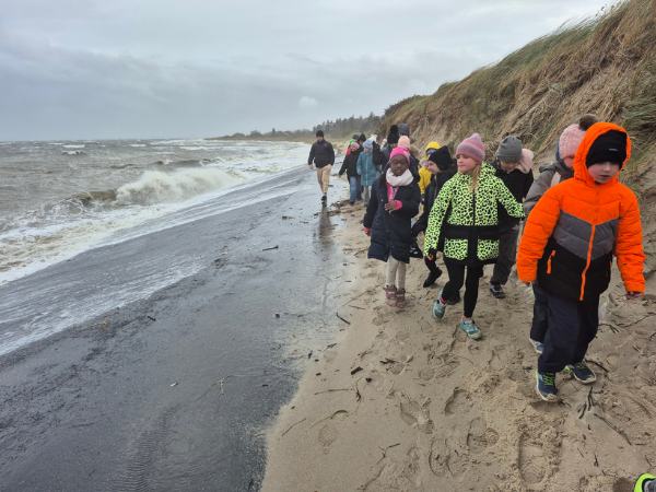 Föhr Herbstreise Spaziergang Warm eingepackte Kinder laufen an einem stürmischen Herbsttag am Meer entlang, vorne läuft ein Kind in neonoranger Jacke