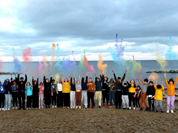 Zirkus-Camp am Strand Eine Gruppe Jugendlicher und Betreuer steht am Strand und wirft bunte Holy Farben in die Luft