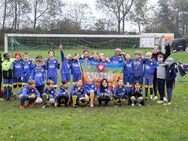 Fußball-Camp Gruppe Gruppe von Kindern in Fußballkleidung steht vor einem Tor, in der Mitte hält eine Kindergruppe eine Fahne hoch auf der Moin steht