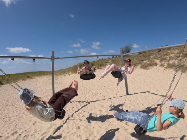 Amrum - Schaukel Vier Mädchen schaukeln auf einem Spielplatz, unter ihnen ist Sand und die Sonne scheint