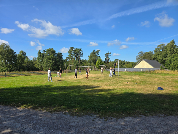 Eine Gruppe Jugendlicher spielt auf einer Wiese vor einem Haus Volleyball